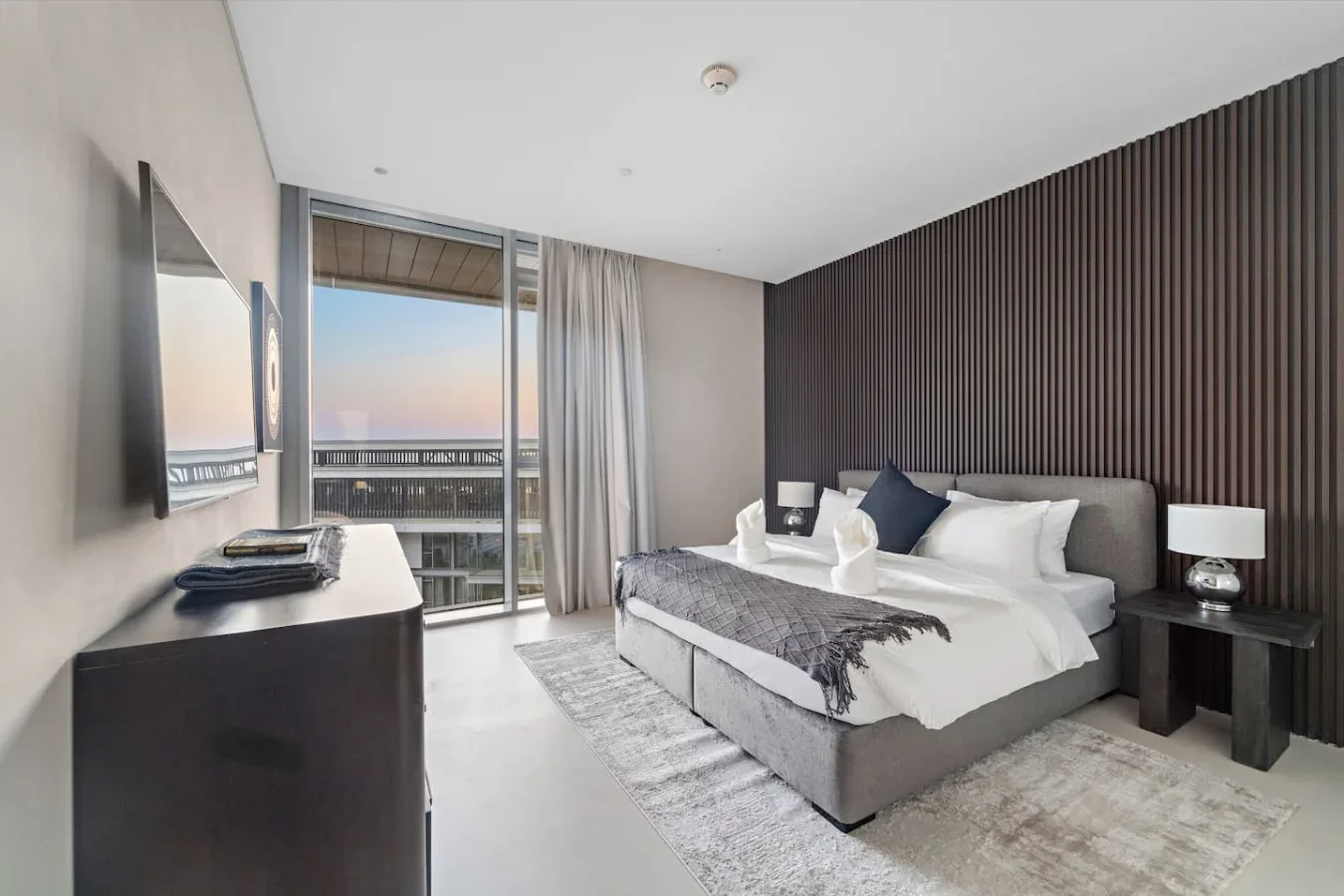 Un dormitorio con una cama, mesillas de noche y una ventana con vistas a edificios cercanos.