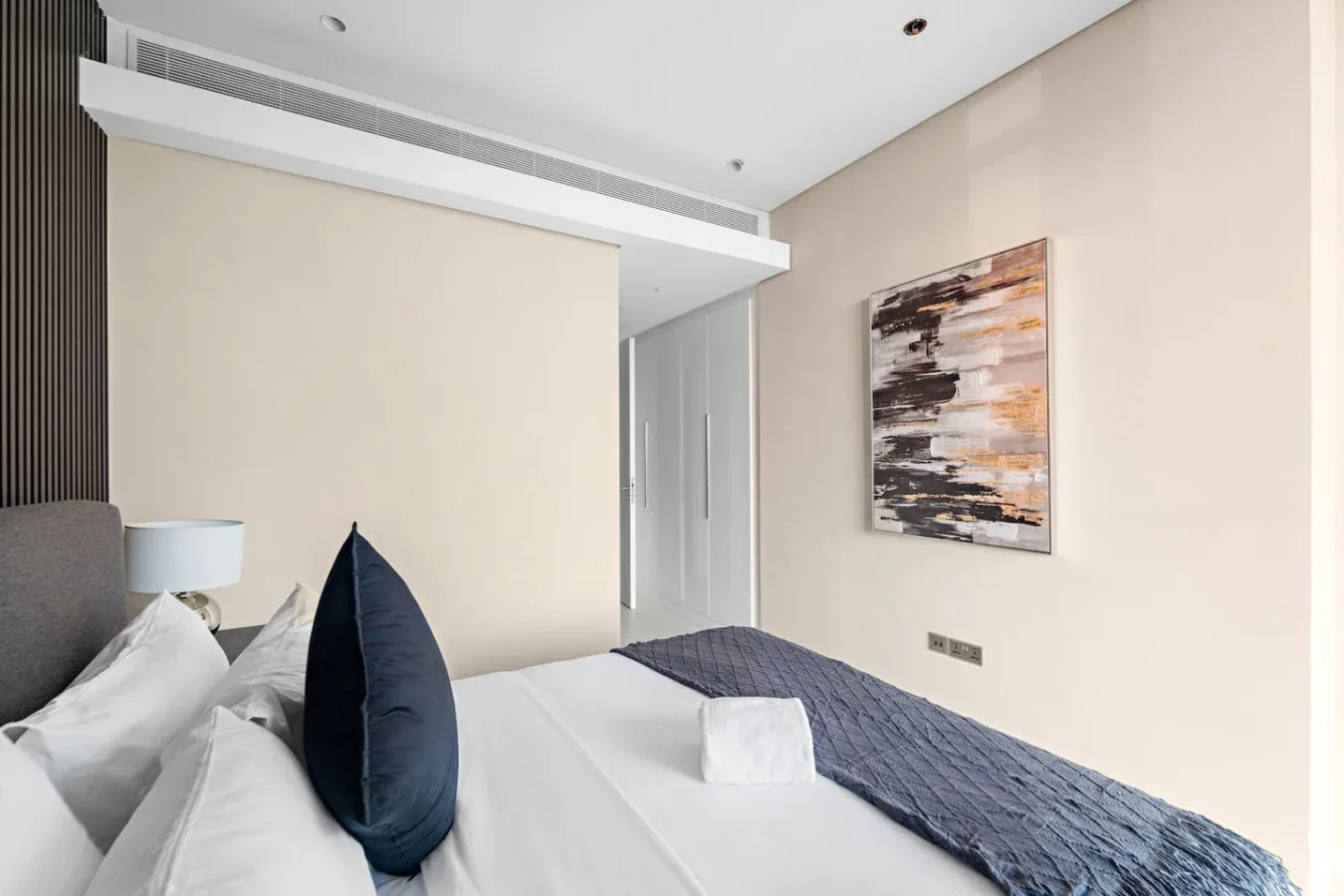 Un dormitorio con ropa de cama blanca, almohadas oscuras y arte abstracto en la pared.