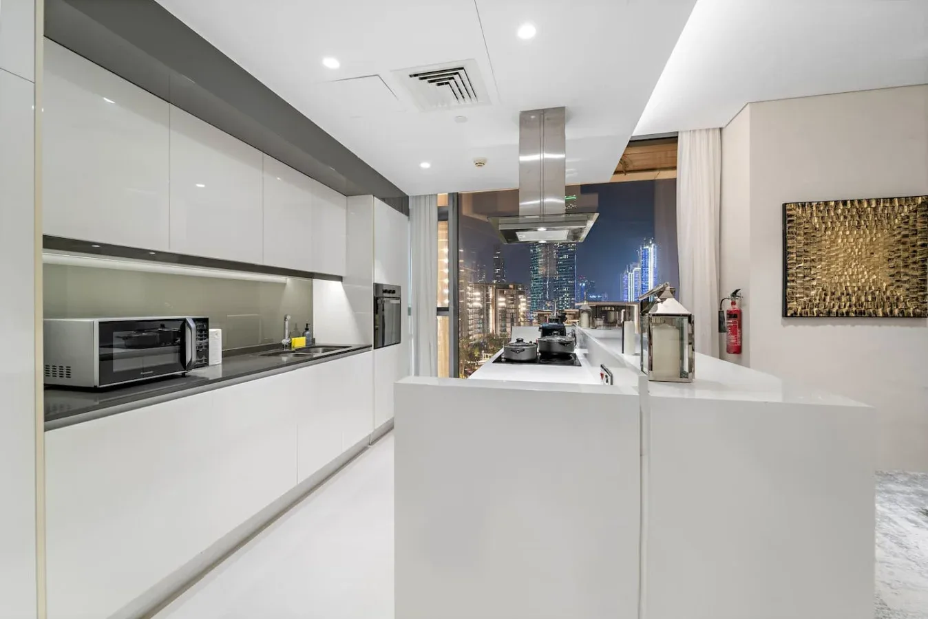 Una cocina moderna con una isla central y luces de la ciudad visibles por las ventanas.