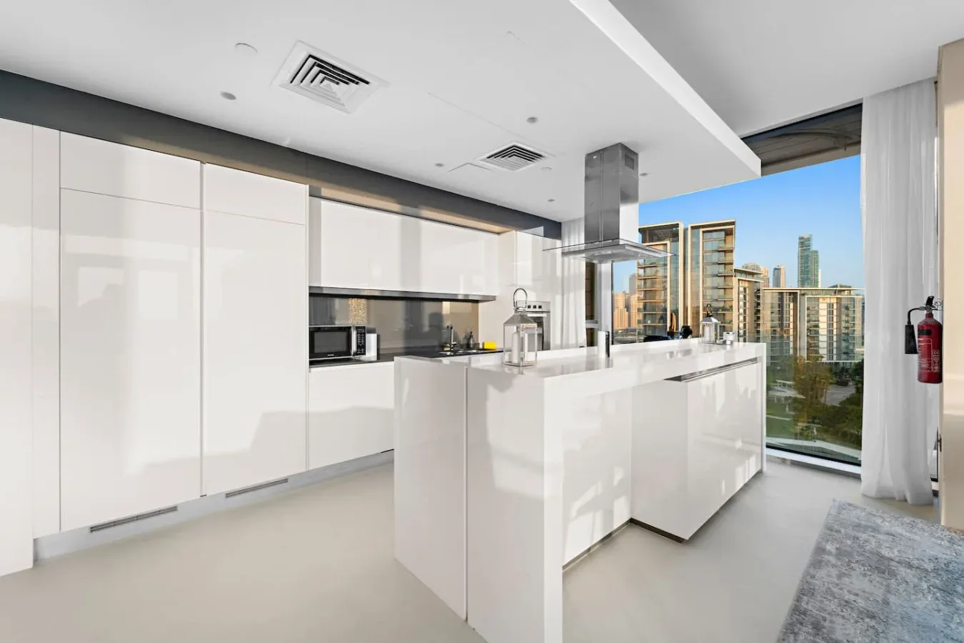 Una cocina moderna con gabinetes blancos y una isla central da a edificios cercanos.