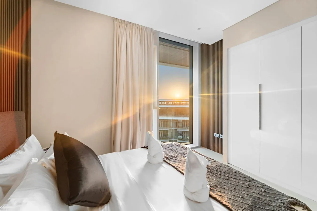 Dormitorio con ropa de cama blanca, una ventana amplia y vistas al atardecer.