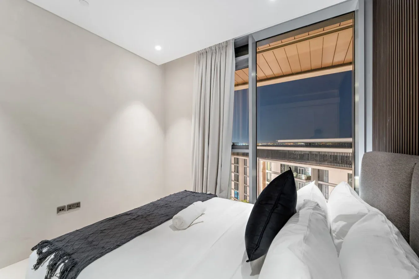 Un dormitorio con una cama bien arreglada junto a una ventana grande.