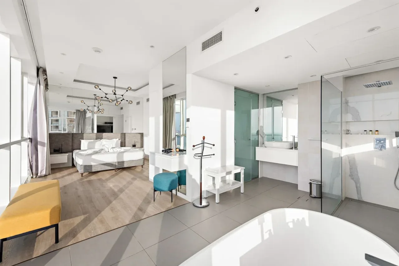 Un dormitorio luminoso se abre a un baño, con una cama y una bañera a la vista.
