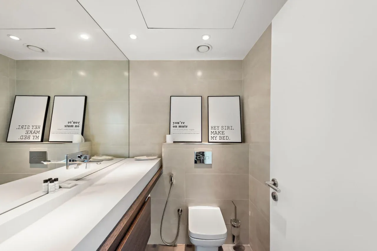 Un baño moderno con inodoro, espejo de pared y lavabo.