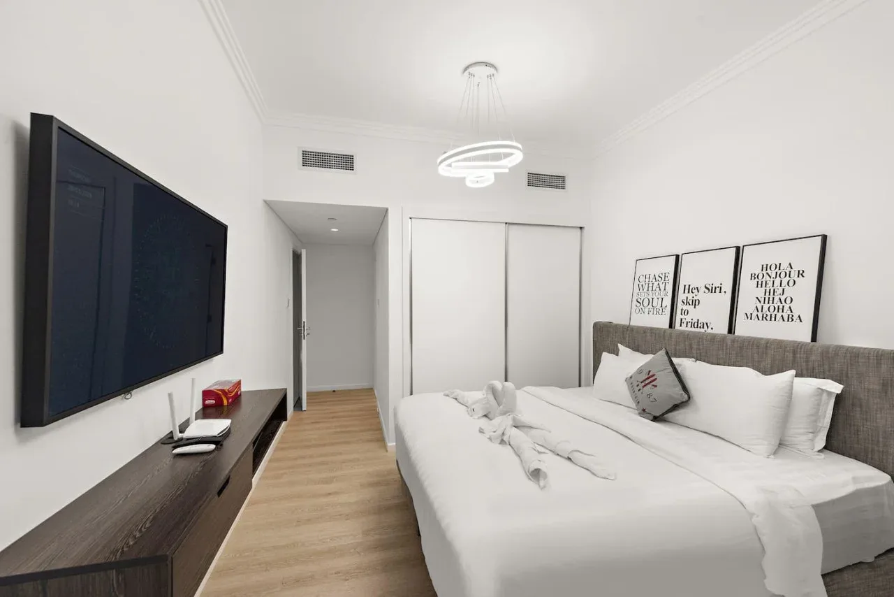 Un dormitorio luminoso con una cama tendida y un televisor montado en la pared.