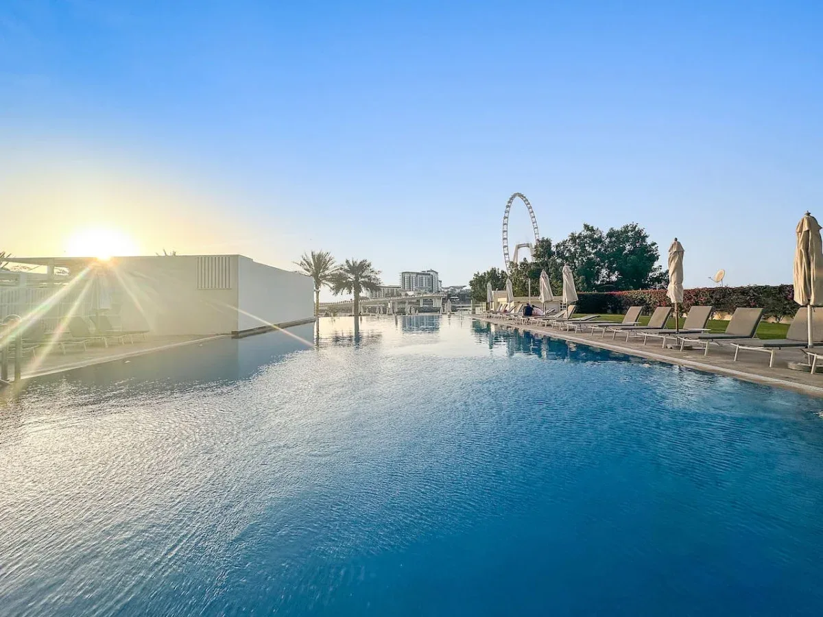 Una piscina al aire libre refleja el sol bajo de la tarde, con tumbonas junto a la terraza.