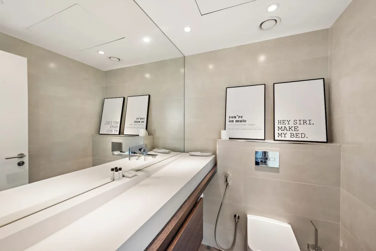 Un baño con un lavabo largo, espejo de pared y láminas enmarcadas.