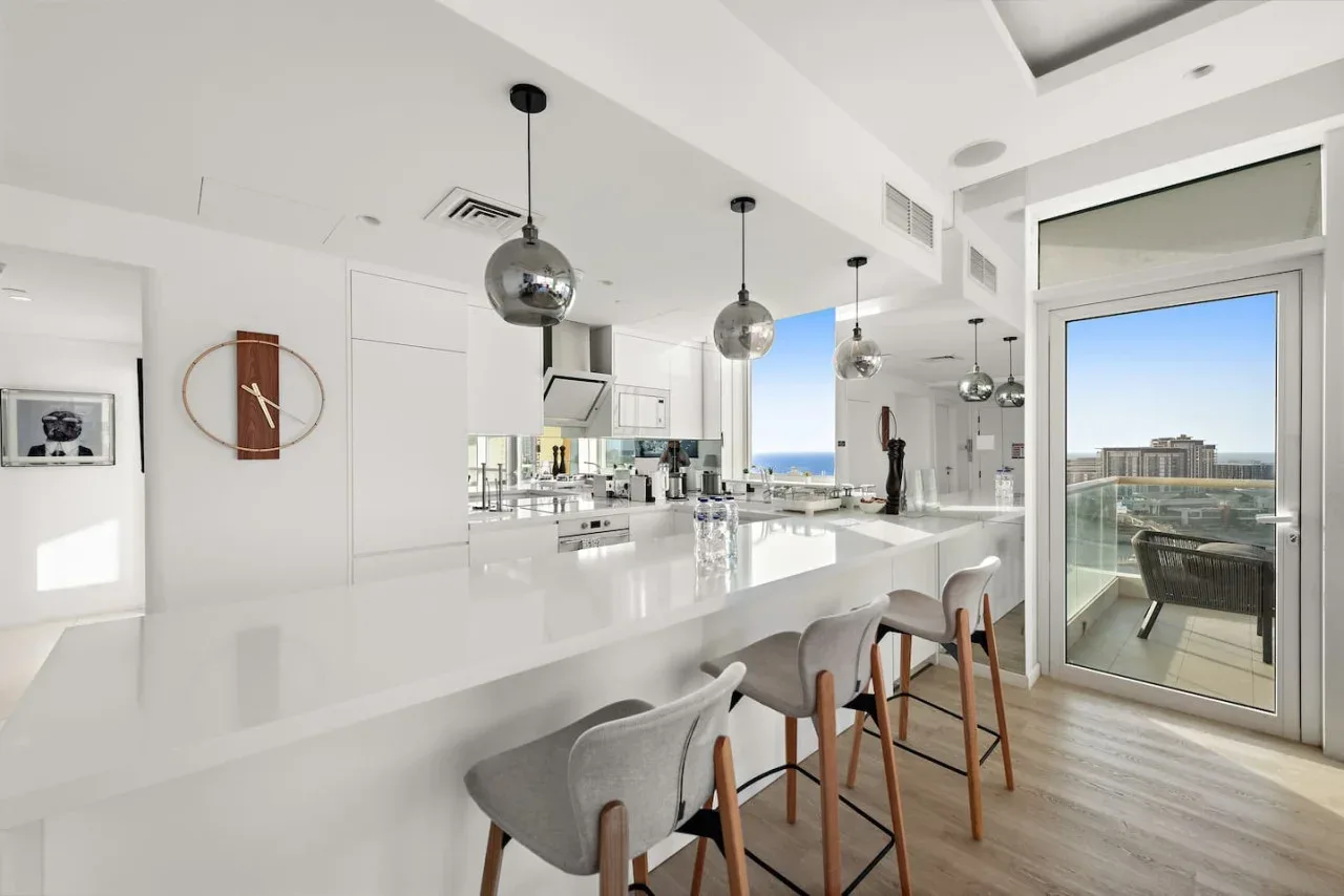 Una cocina luminosa con una isla larga y asientos junto a puertas de vidrio.