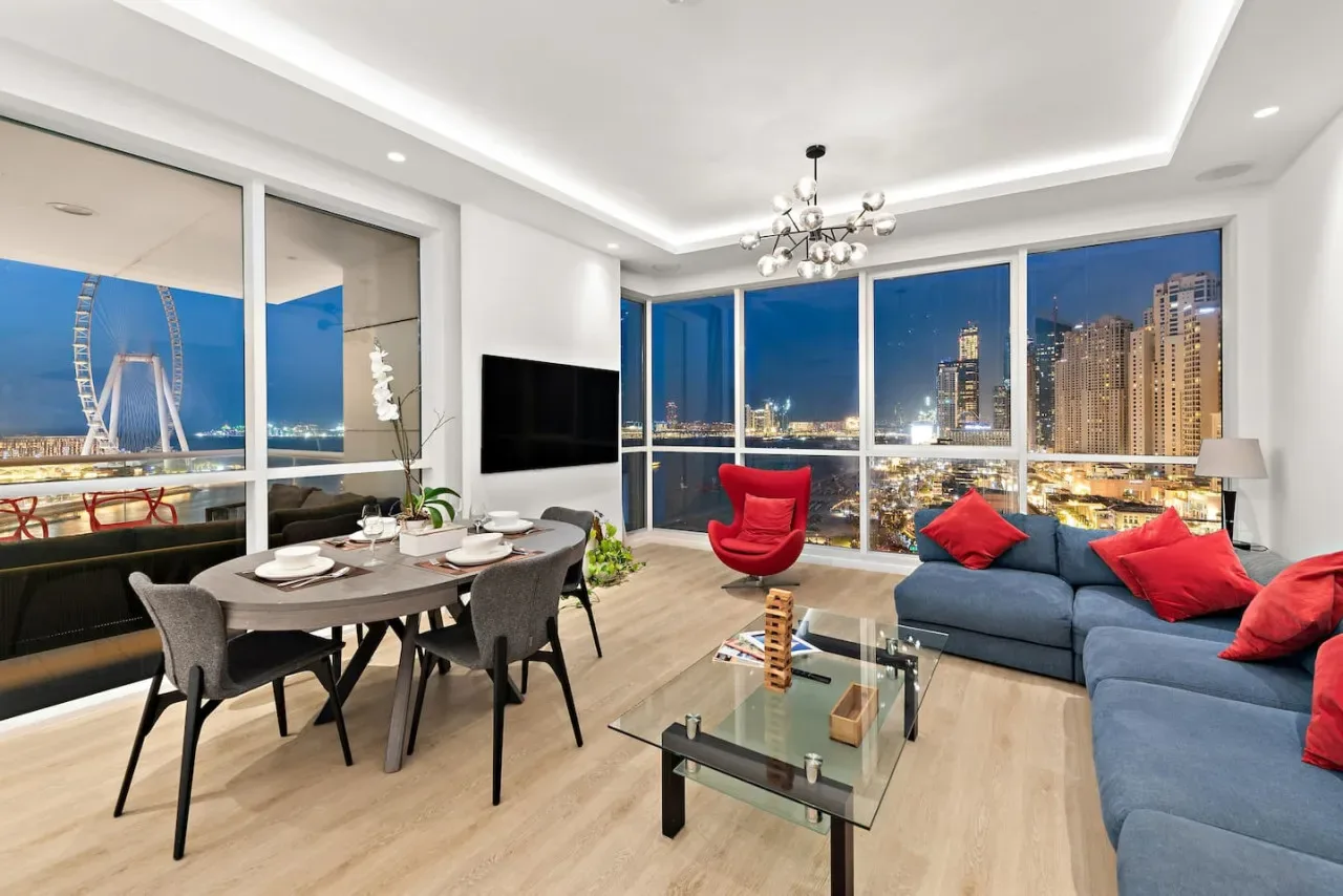 Una sala moderna tiene una mesa de comedor y asientos junto a grandes ventanas con vistas a la ciudad de noche.