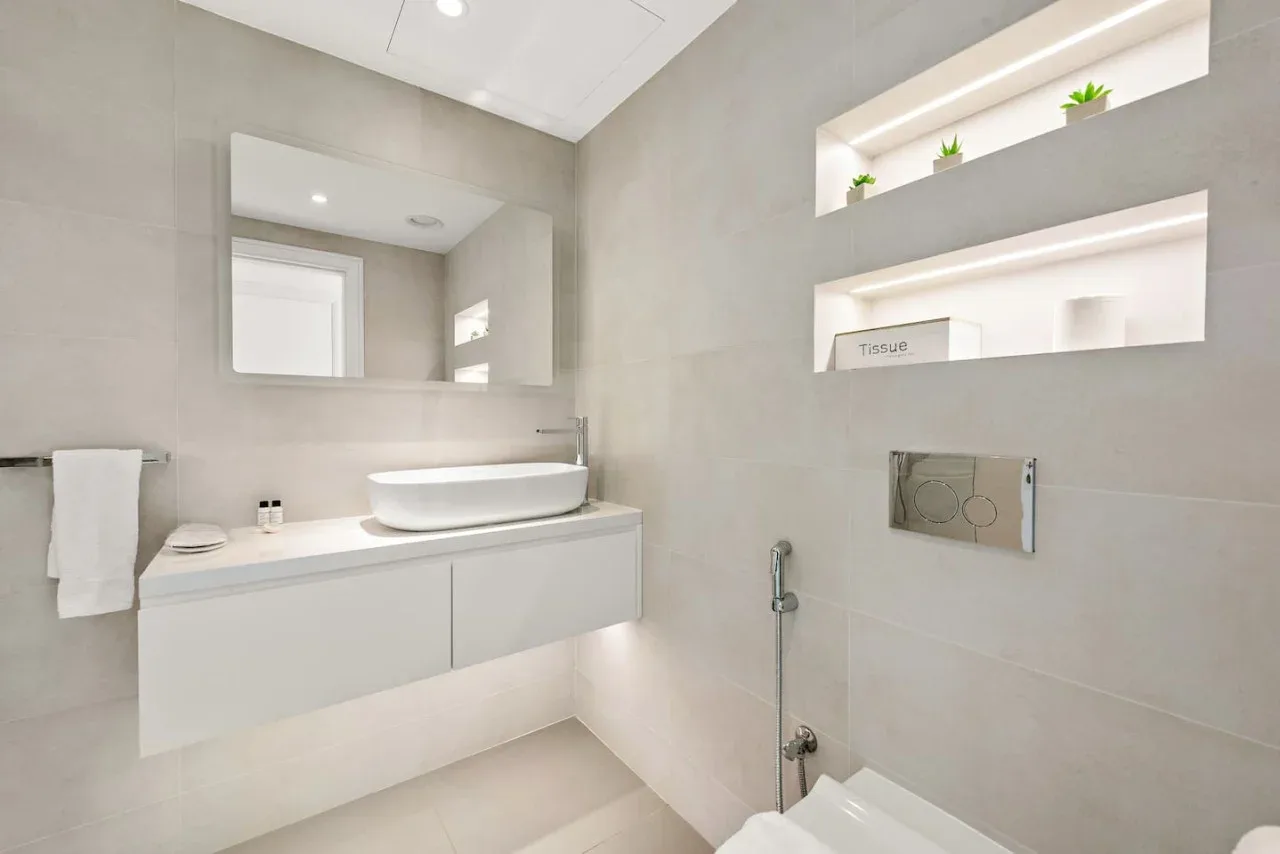 Un baño moderno con un lavabo suspendido, un lavamanos sobrepuesto y nichos iluminados.