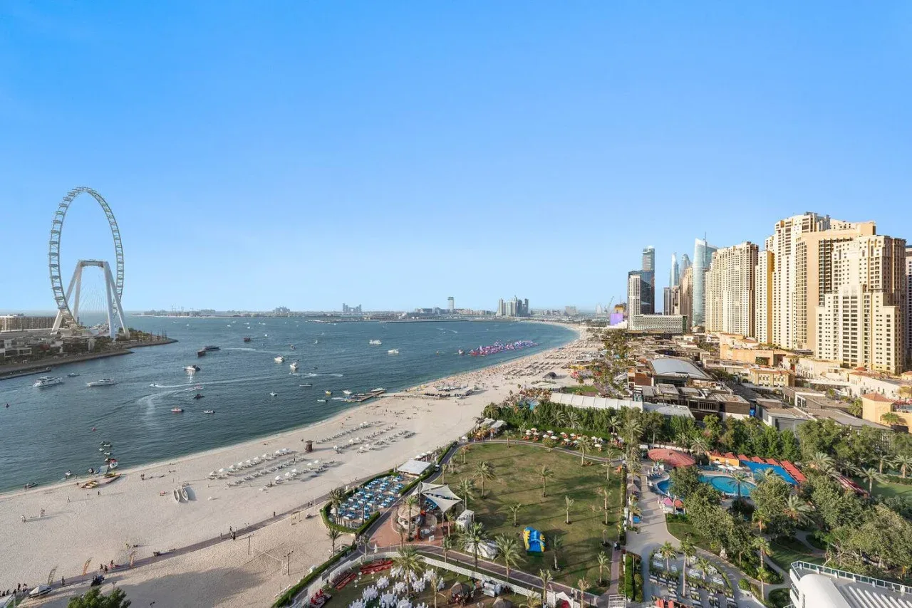 Paisaje urbano costero con una playa de arena, edificios junto al agua y una gran noria.
