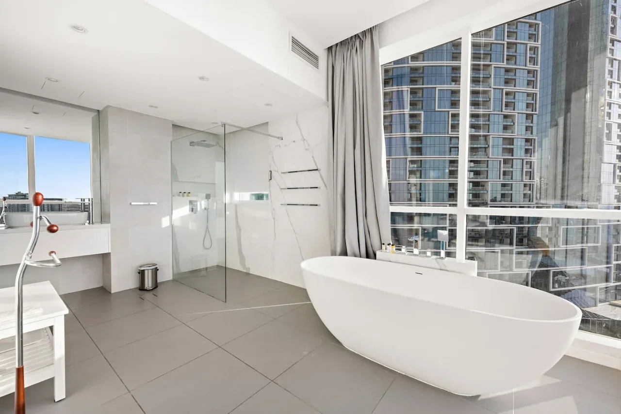 Un baño luminoso tiene una bañera independiente junto a grandes ventanales.