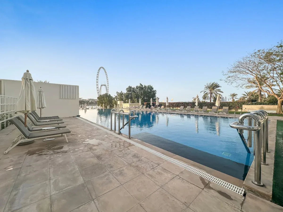 Una piscina al aire libre está rodeada por una terraza pavimentada y asientos.