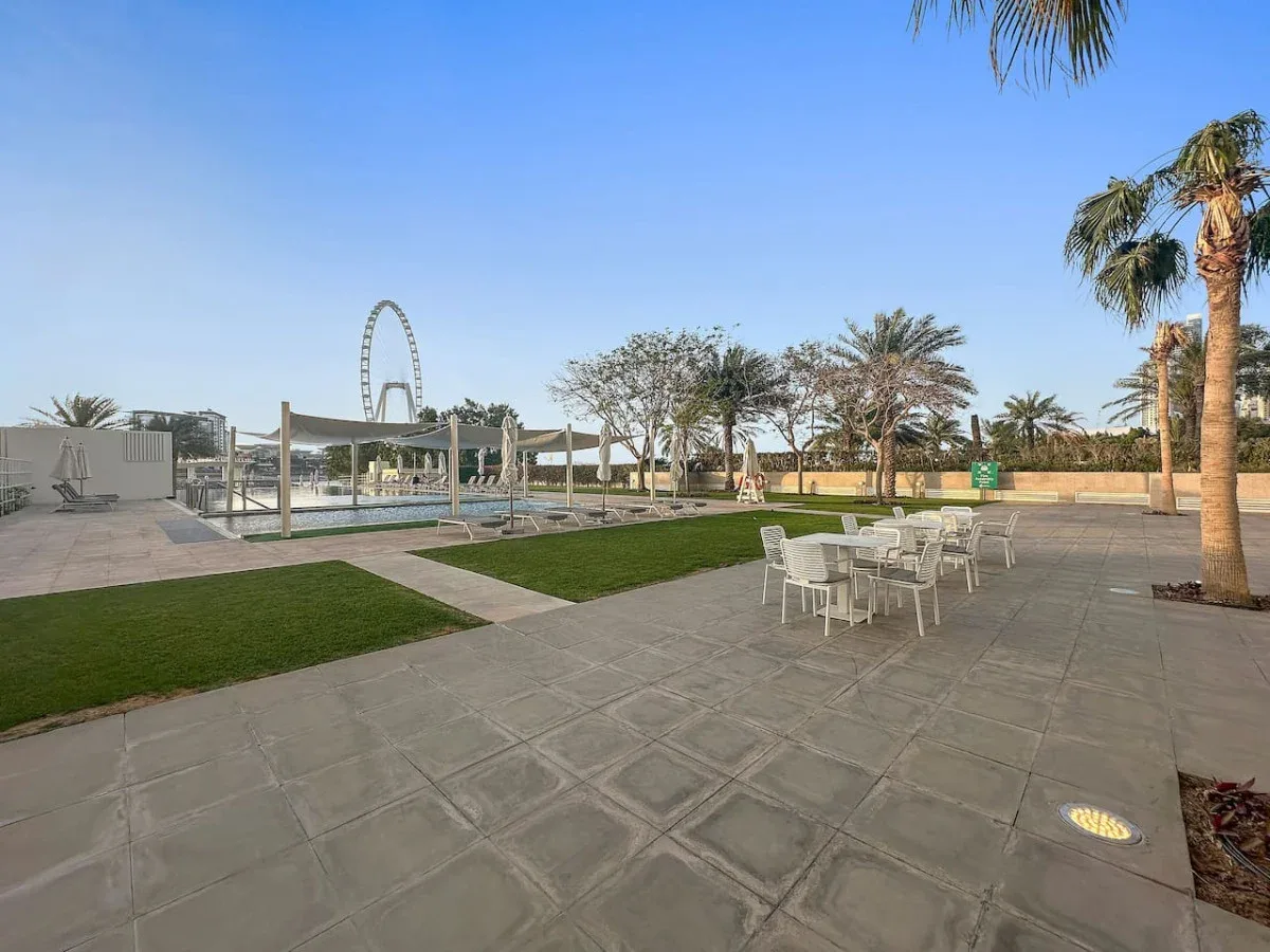 Una zona de piscina al aire libre tiene asientos sobre pavimento, césped y palmeras.