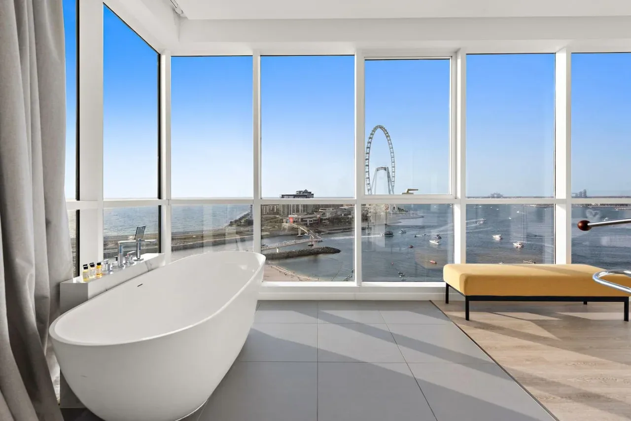 Una bañera exenta está junto a ventanales con vistas al paseo marítimo.