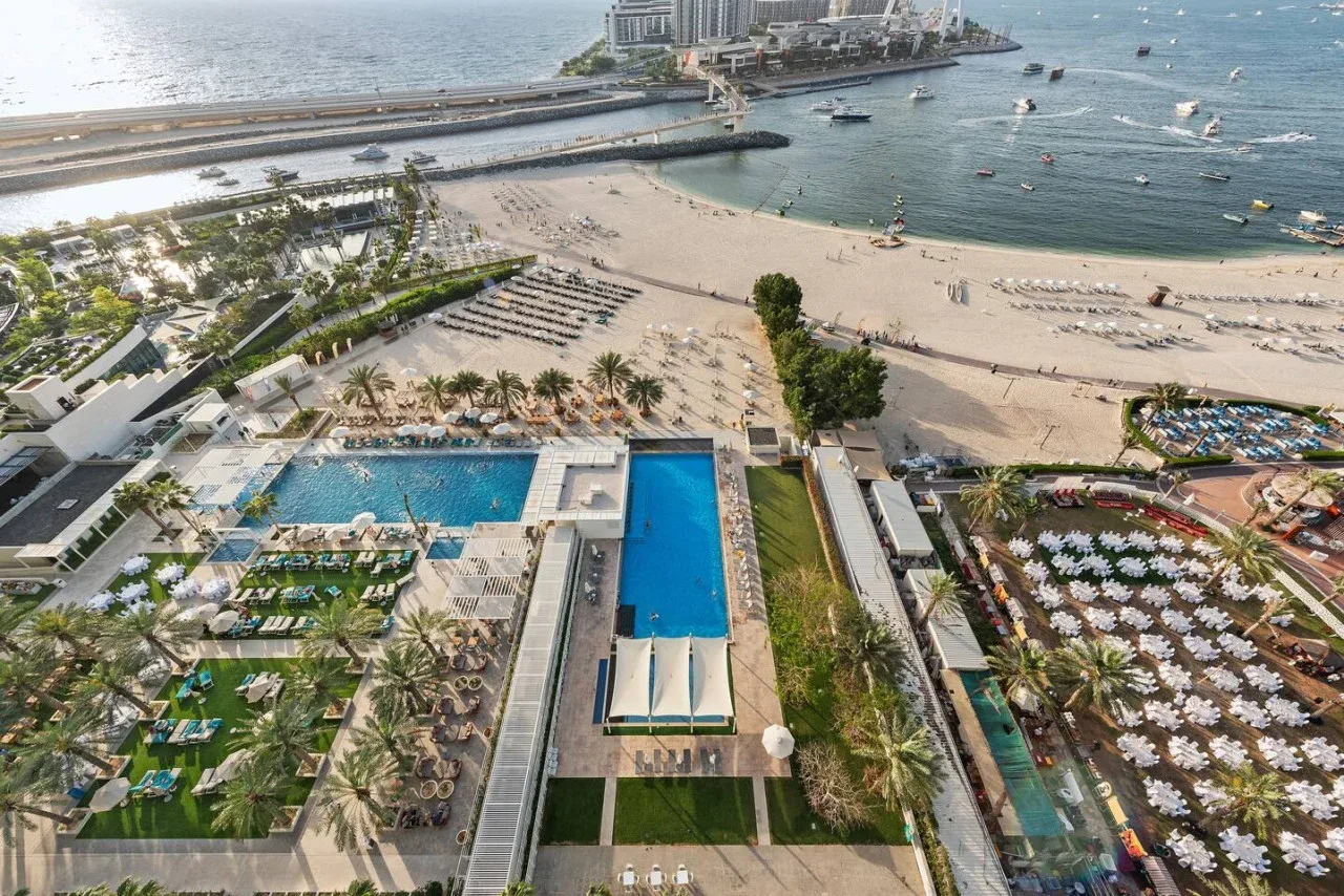 Vista aérea de un complejo junto a la playa, con piscinas, jardines y el mar.