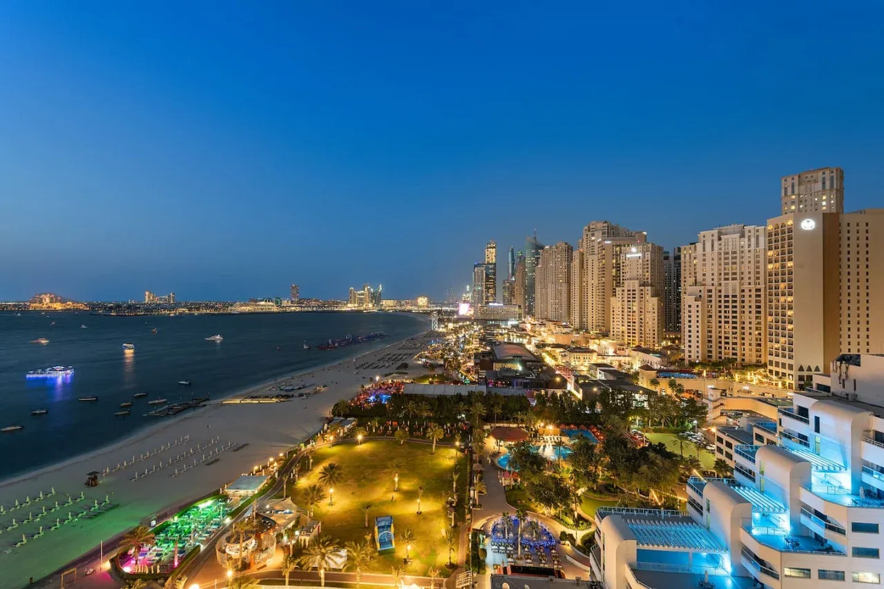 Un paseo marítimo urbano al anochecer, con edificios altos junto a la costa.
