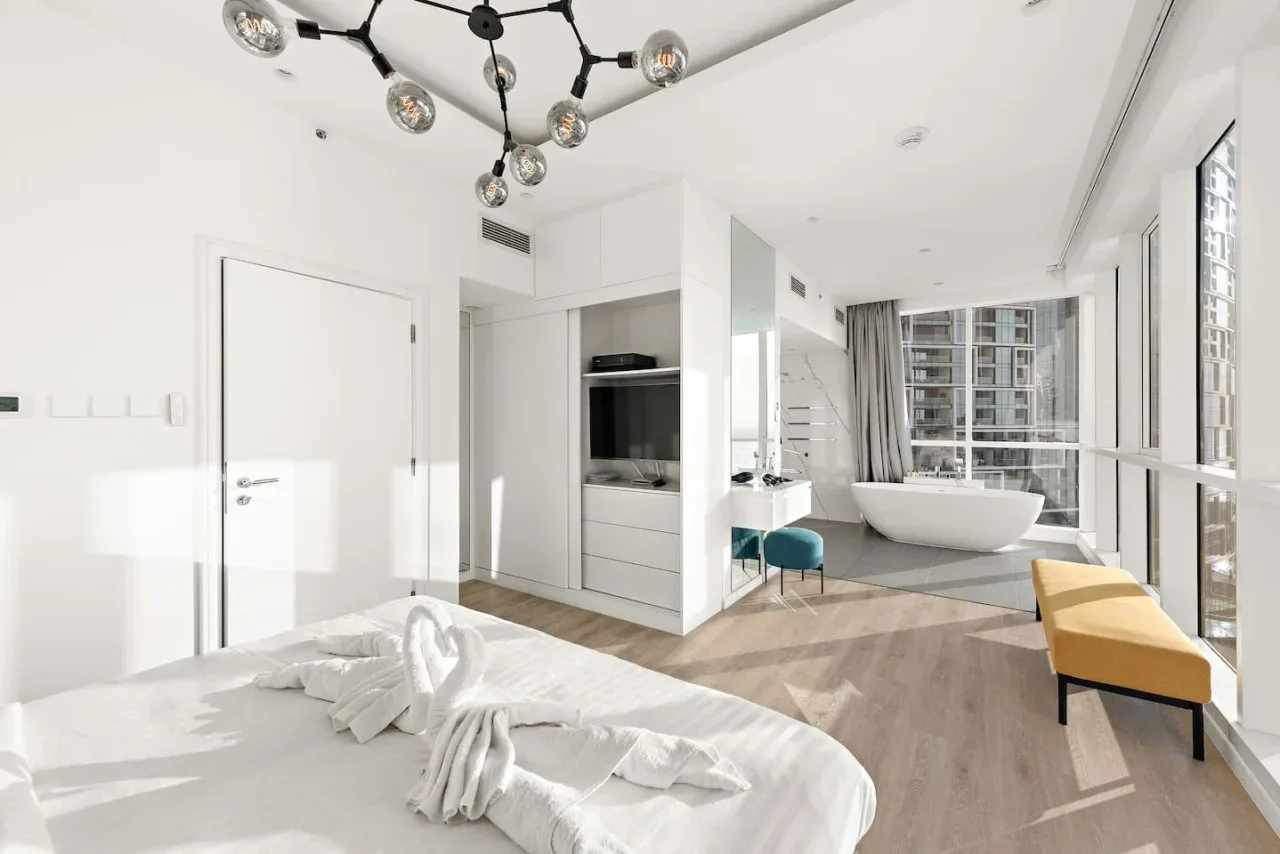 Un dormitorio luminoso se abre a una bañera junto a grandes ventanales.