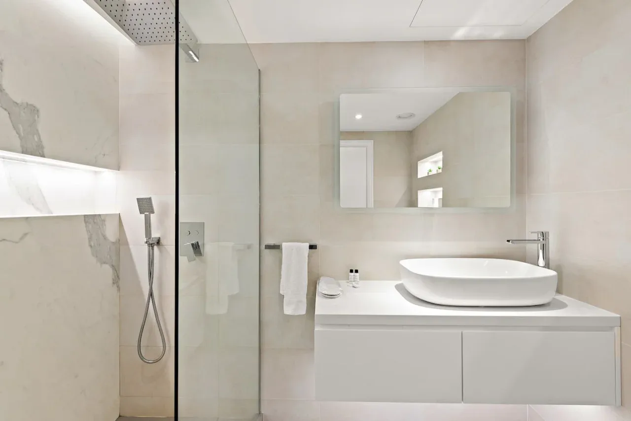 Un baño luminoso con ducha de vidrio y un amplio tocador bajo un espejo.