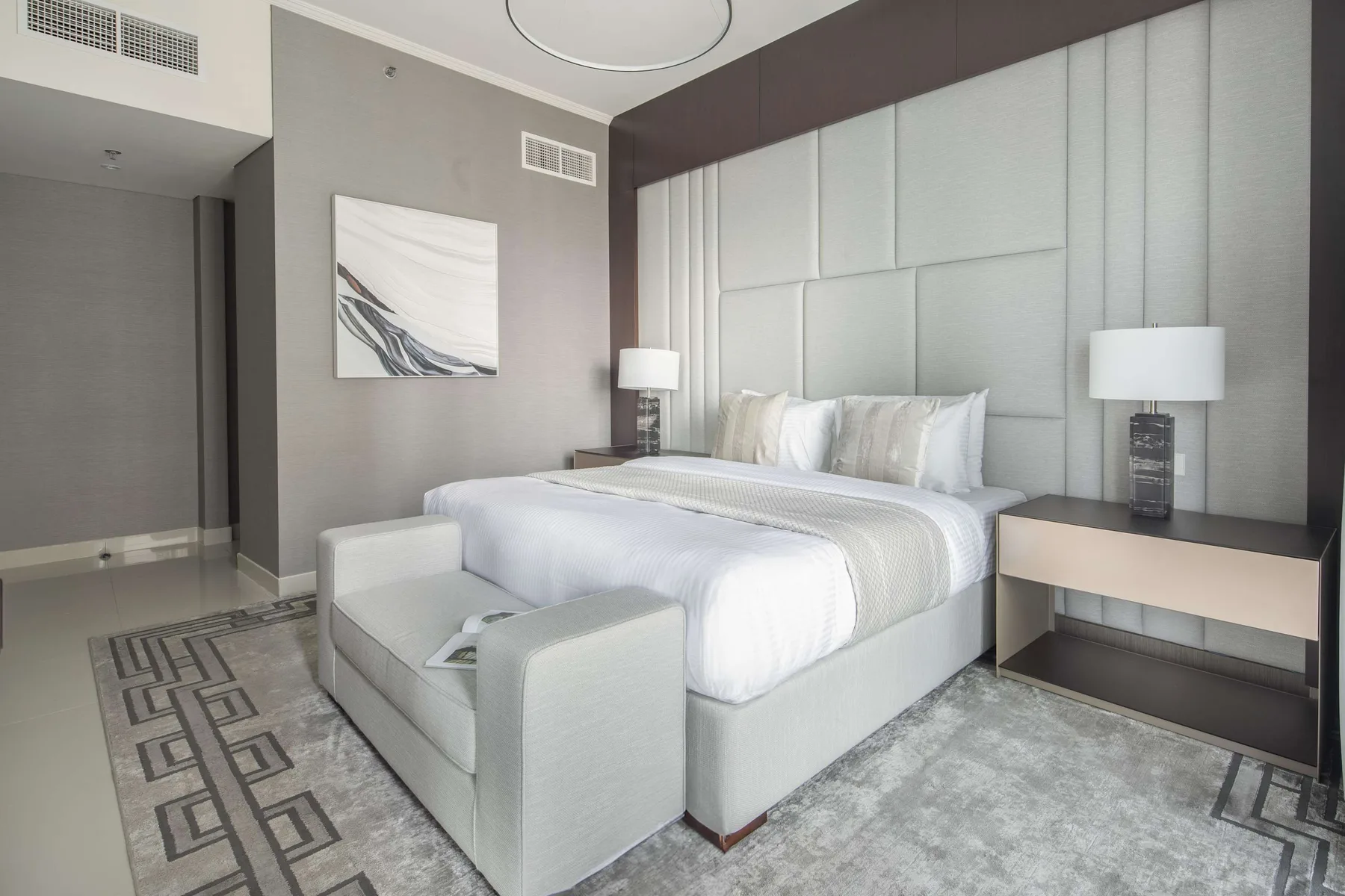 Un dormitorio moderno con una cama grande, asientos tapizados y arte abstracto en la pared.
