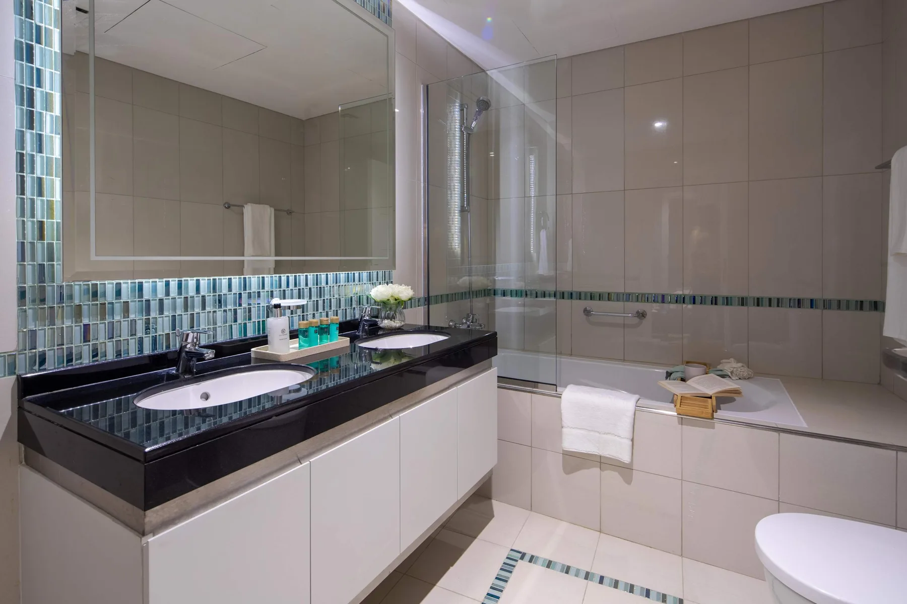 Un baño alicatado con lavabo doble, bañera y ducha de cristal.