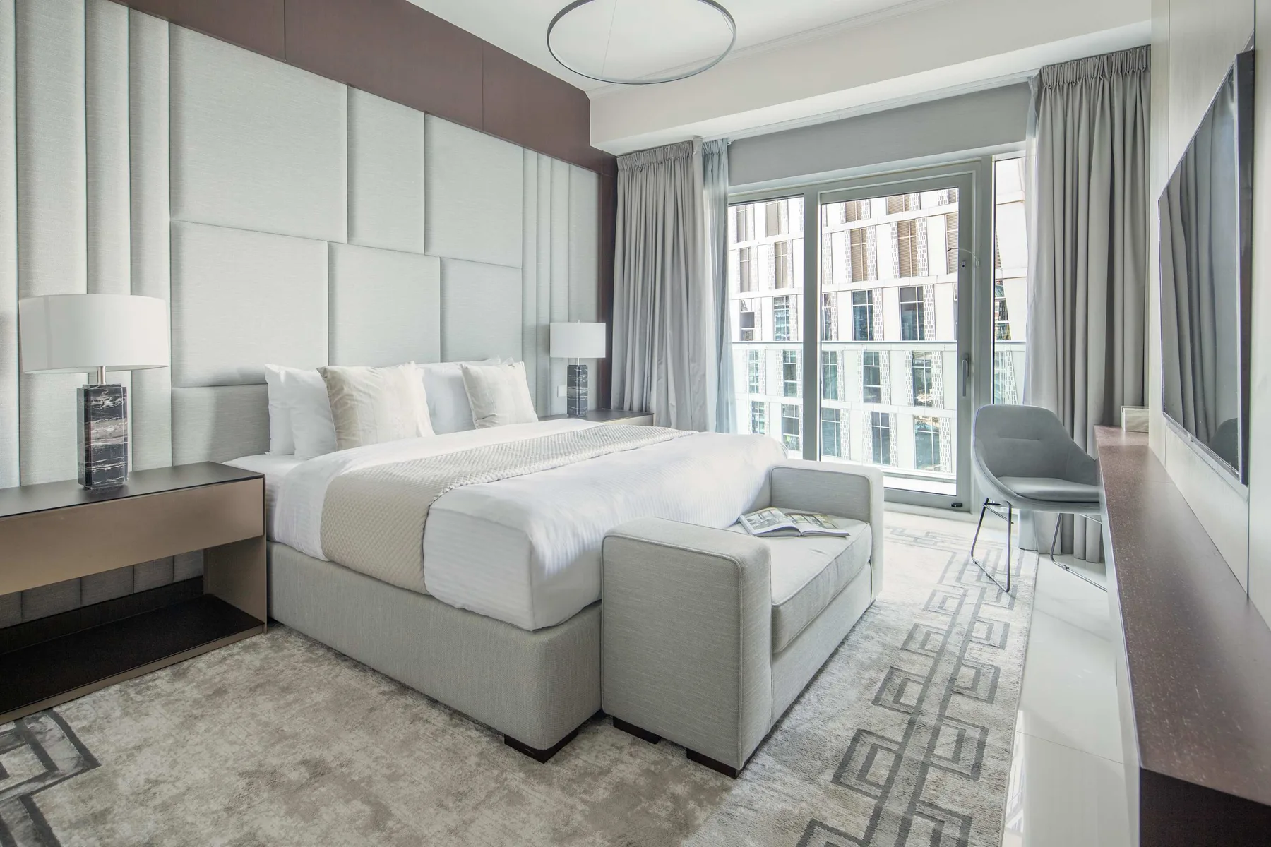 Un dormitorio luminoso con una cama tendida y grandes ventanas.