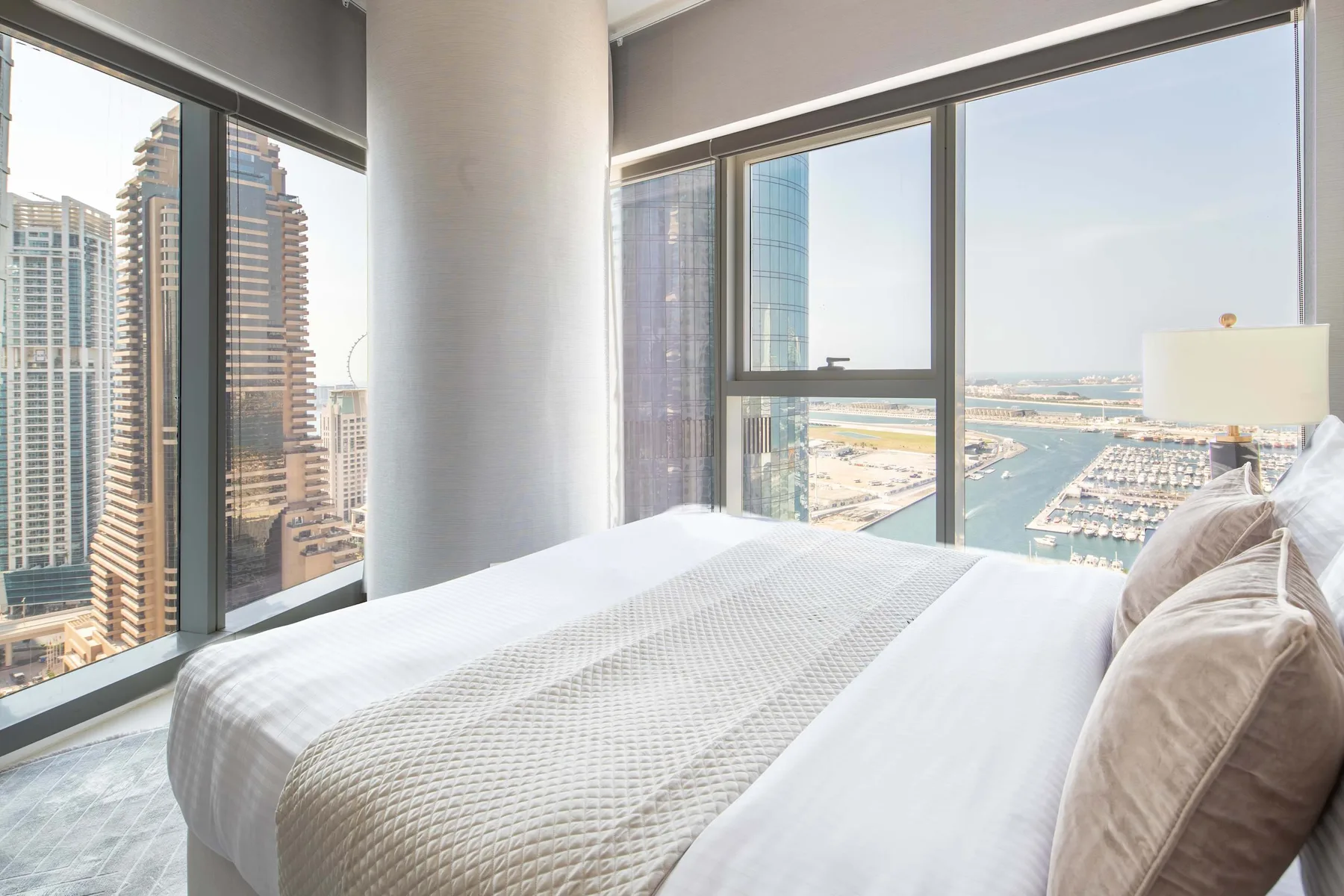 Un dormitorio con una cama bien tendida junto a grandes ventanas con vistas al paseo marítimo.