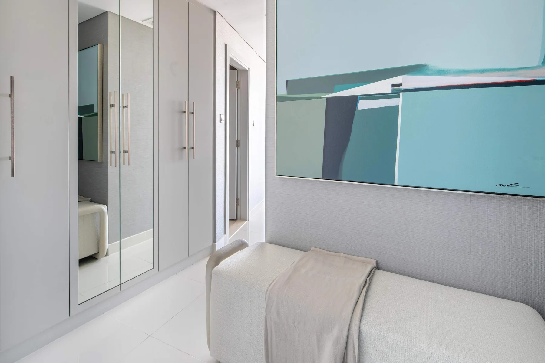 Un dormitorio luminoso con armarios con espejo y una cama bajo una obra abstracta colorida.