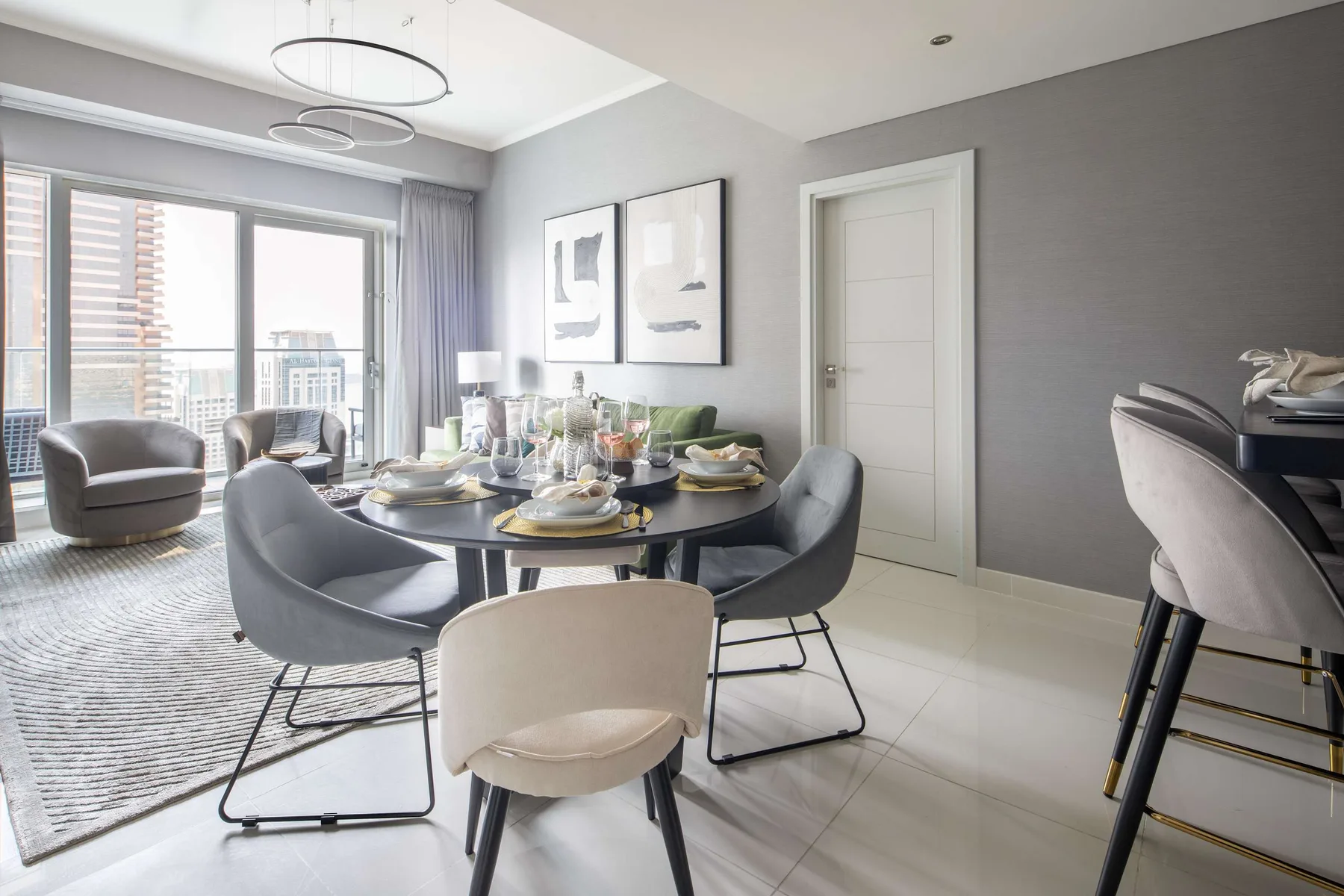 Un comedor luminoso con la mesa puesta junto a grandes ventanas y una zona de estar.