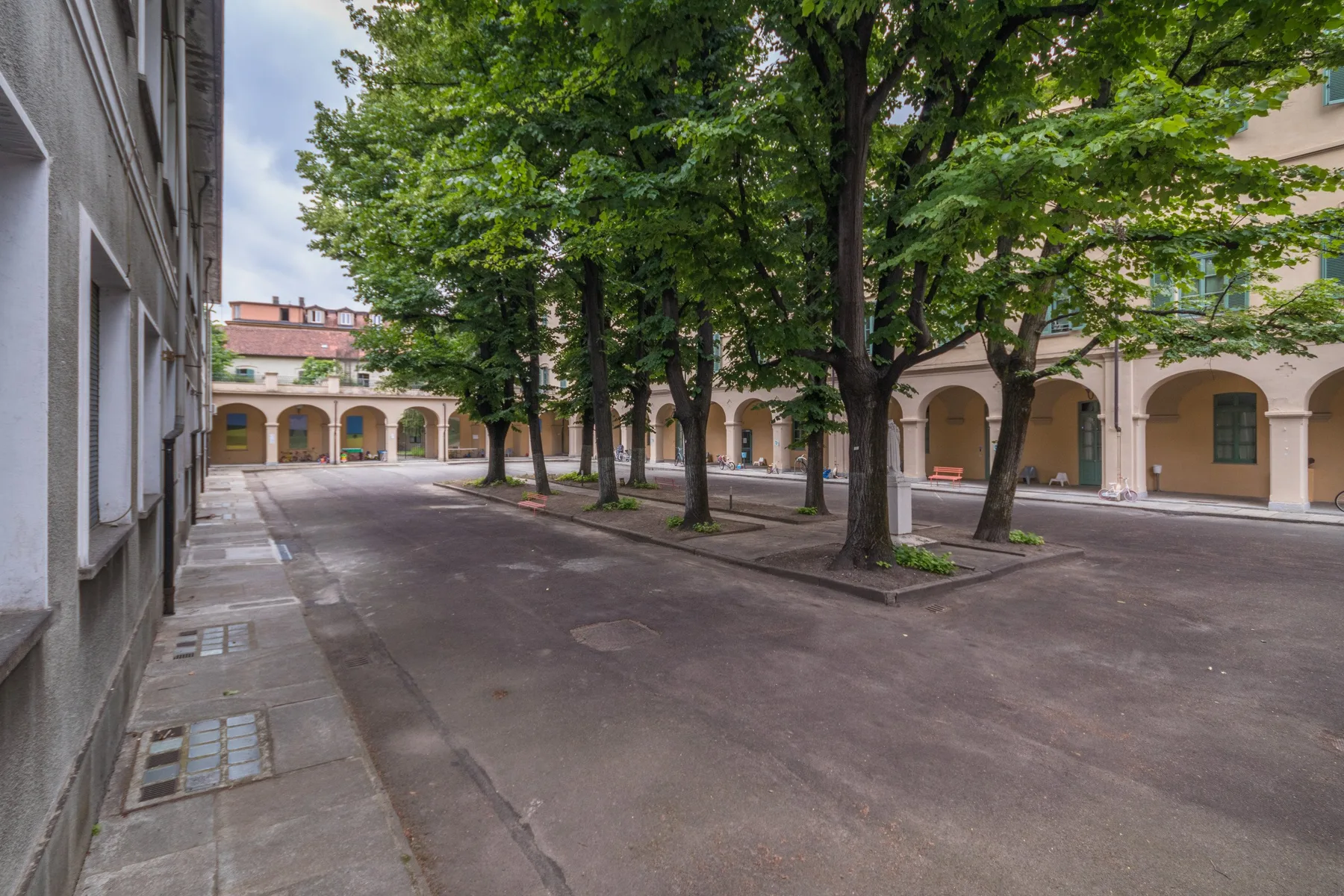 Un patio pavimentado con árboles frondosos y pasillos con arcos.