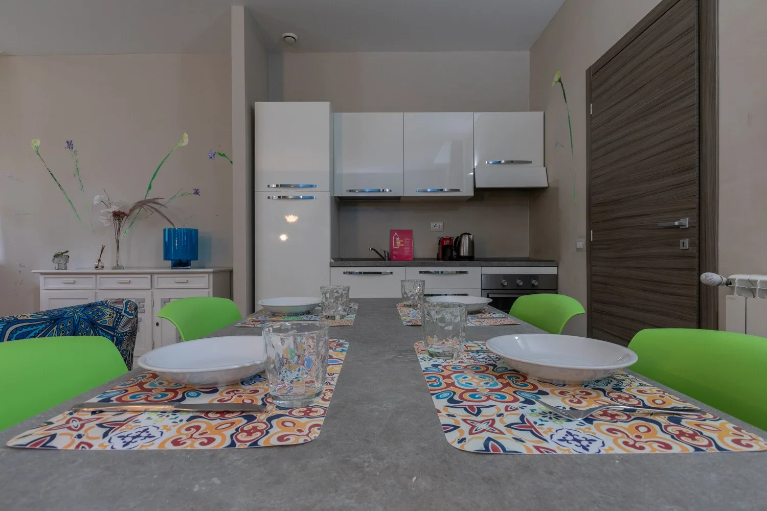 Una mesa de comedor con manteles coloridos está frente a una cocina compacta.