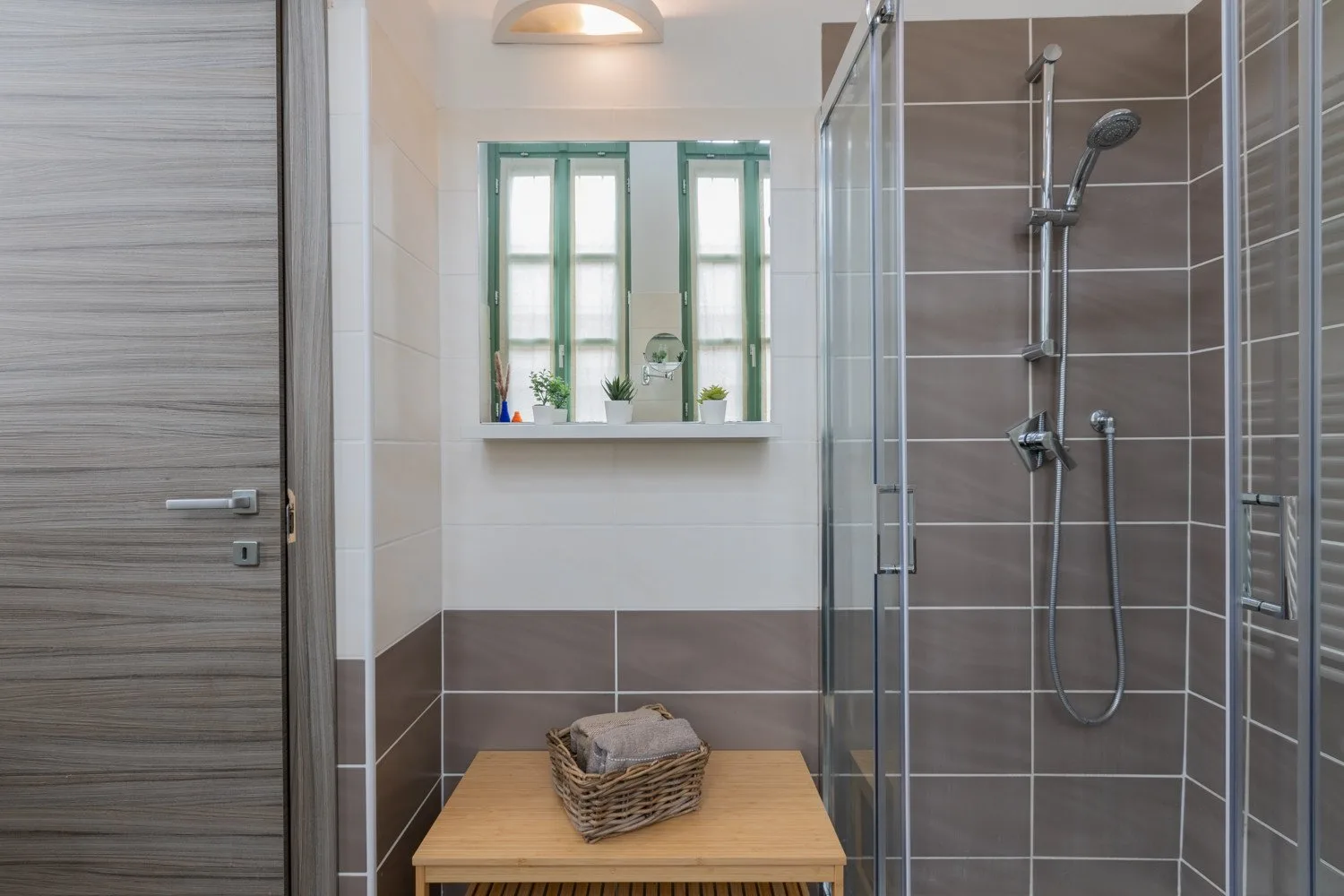 Un baño alicatado con una ducha de vidrio y una ventana pequeña sobre la pared inferior.