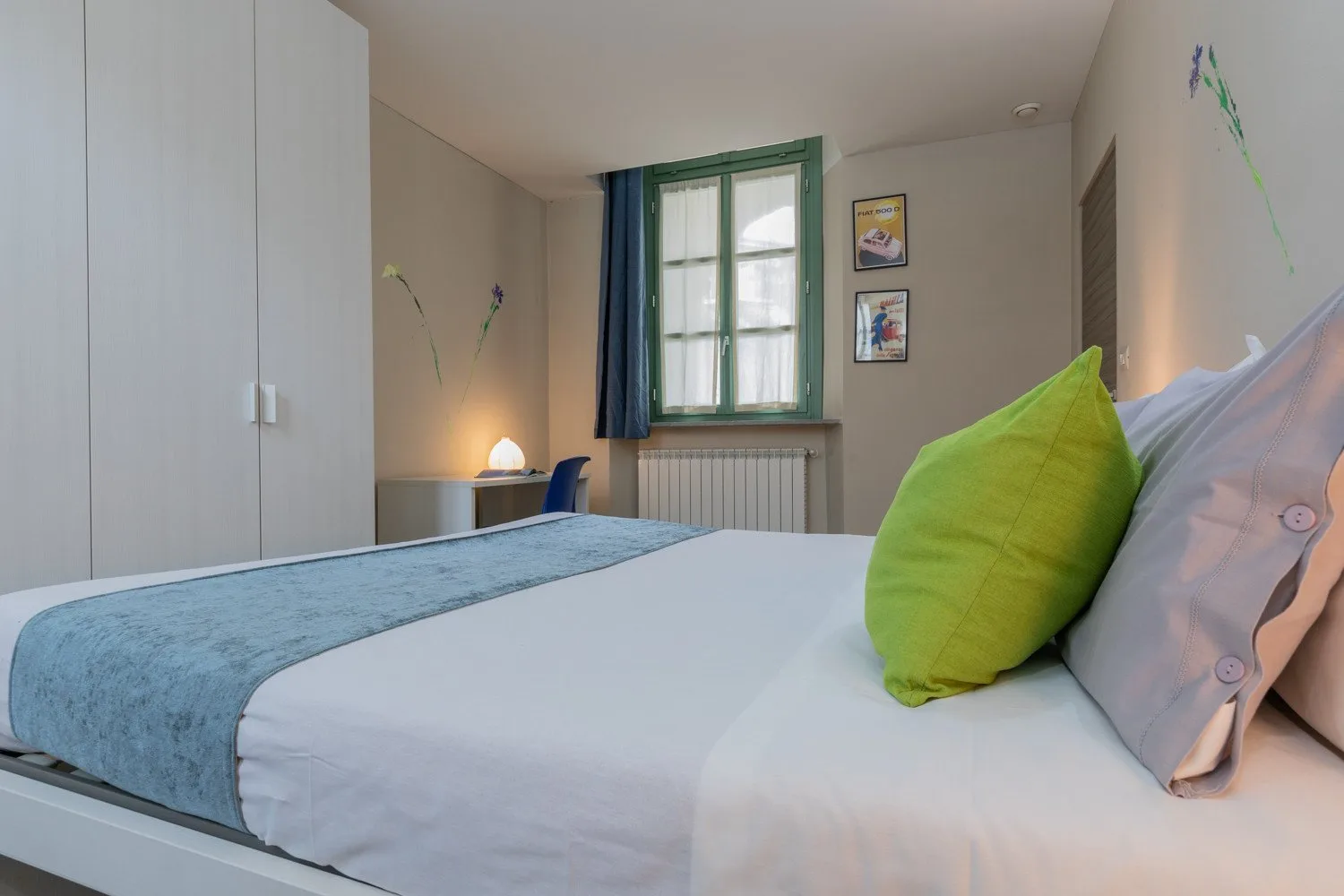 Un dormitorio con una cama tendida, un cojín verde y una ventana.