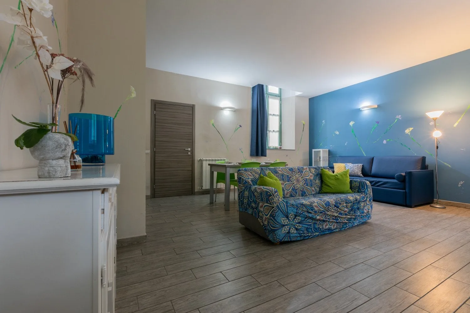 Una sala de estar con un sofá estampado, un sofá azul y una mesa de comedor pequeña.