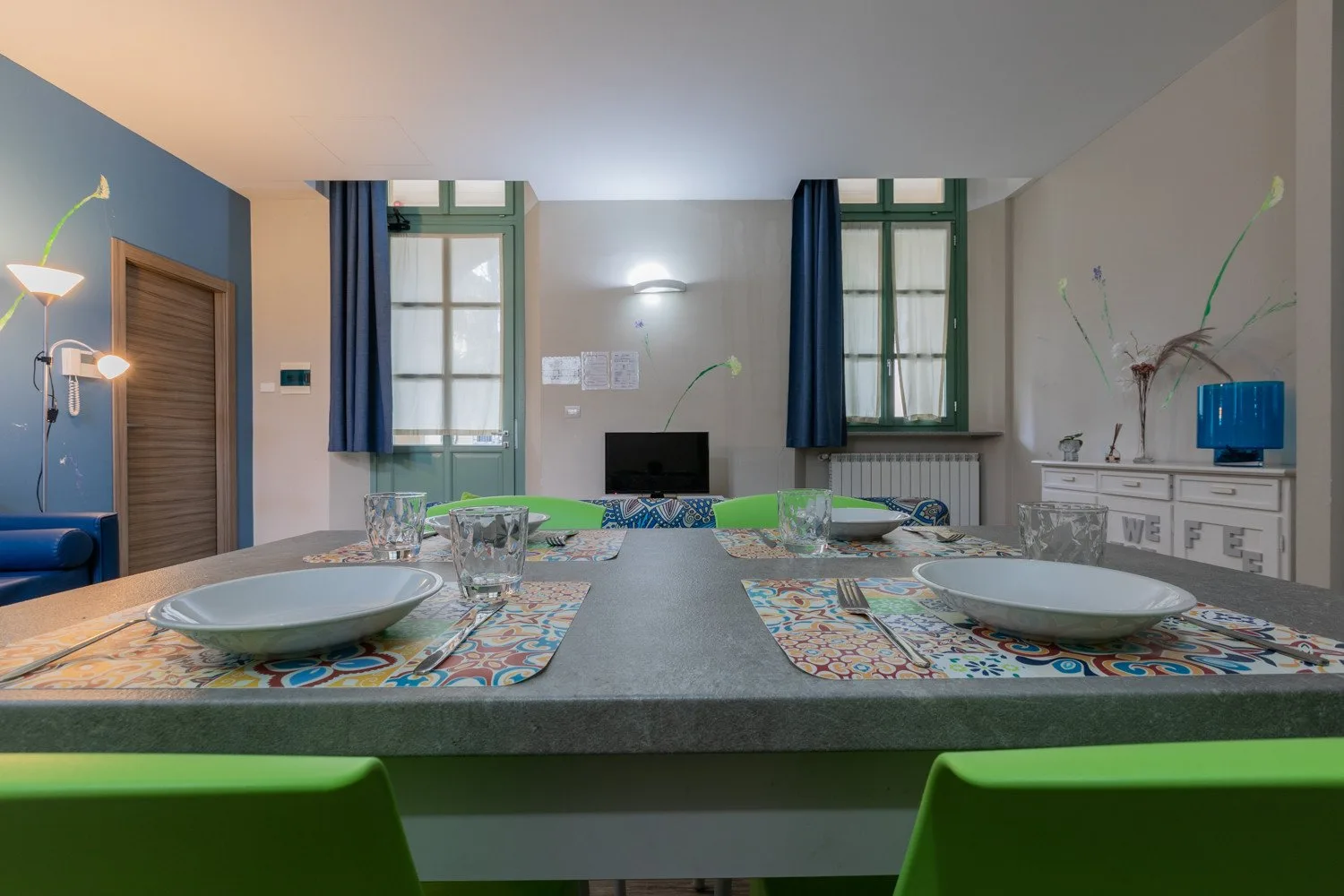 Un comedor con una mesa larga preparada con platos y sillas verdes.