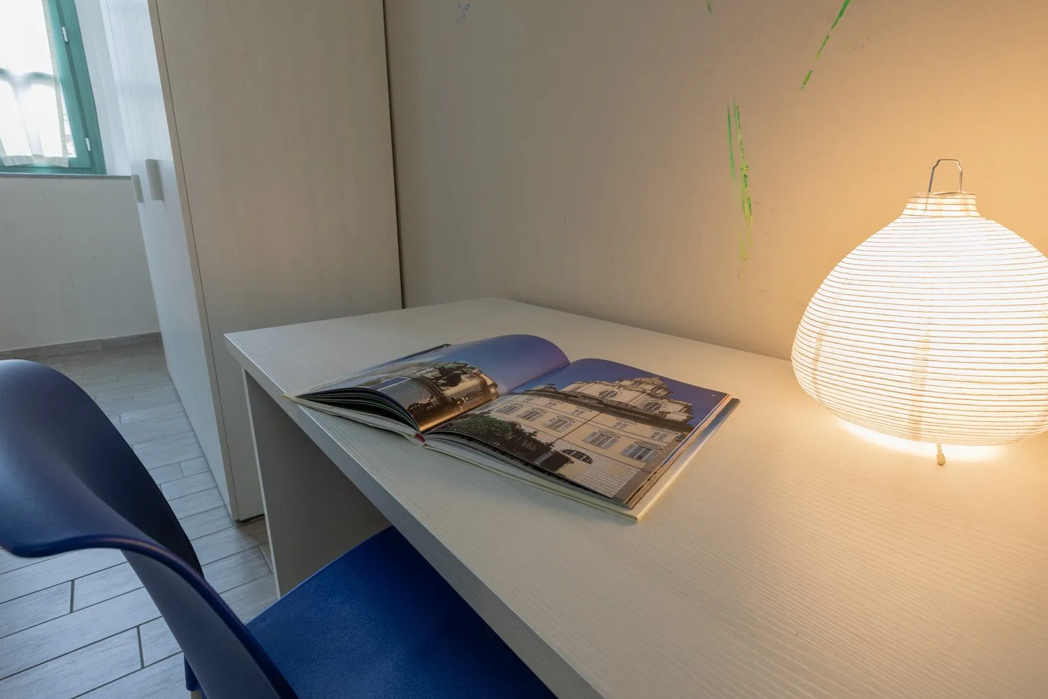 Un escritorio con un libro abierto y una lámpara encendida junto a una ventana.