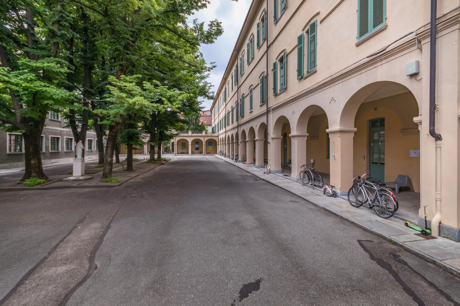 Un patio pavimentado bordea un edificio largo con pasillos en arco y bicicletas estacionadas.