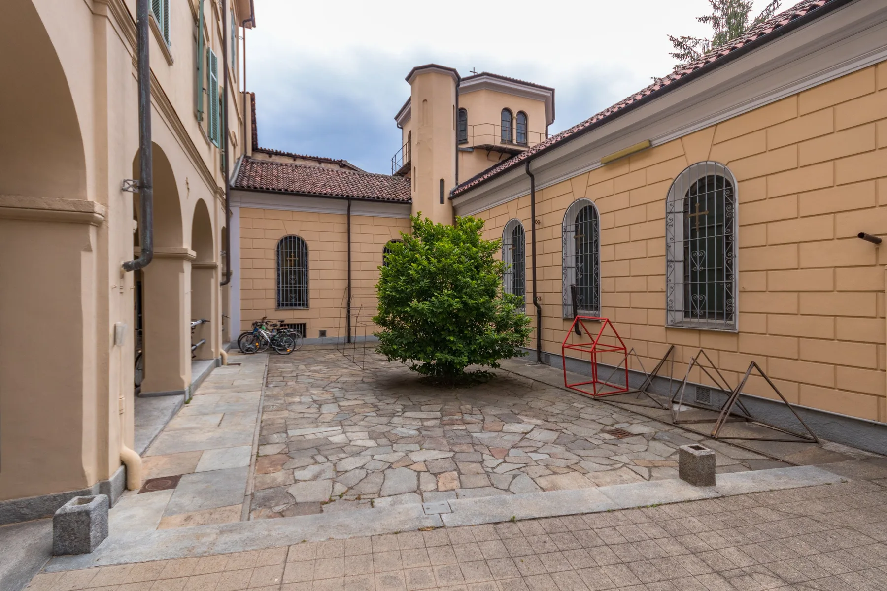 Un patio pavimentado con ventanas arqueadas y un árbol frondoso.
