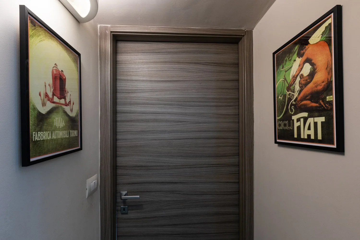 Un pasillo con una puerta de madera cerrada entre dos carteles enmarcados.