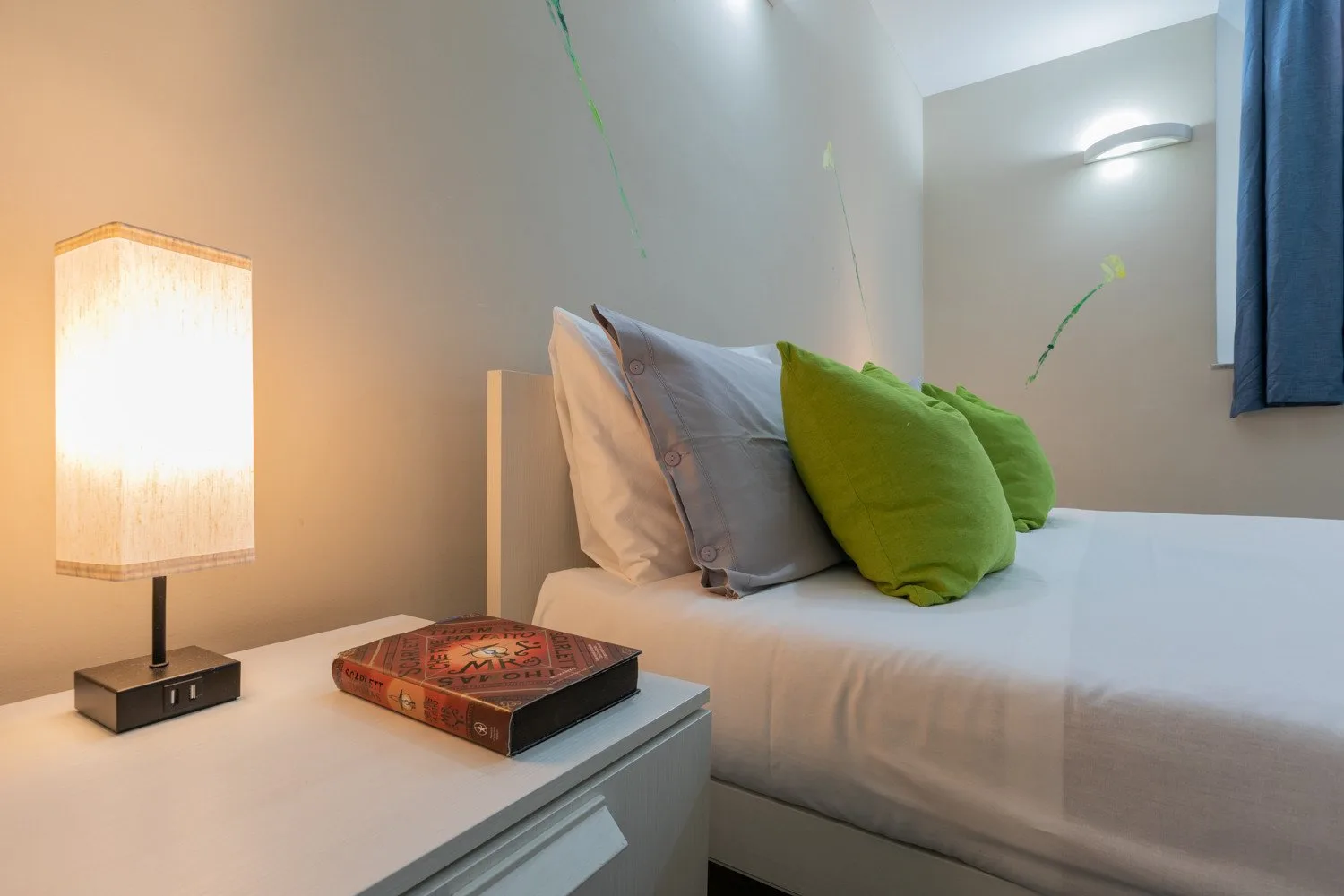 Un dormitorio con una cama tendida y almohadas de colores junto a una lámpara encendida.