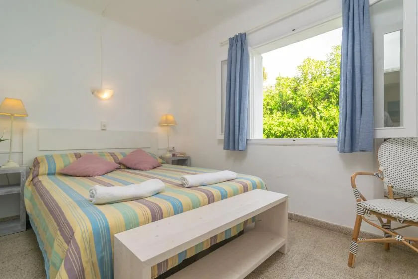 Un dormitorio con una colcha a rayas y una gran ventana con vistas a la vegetación.