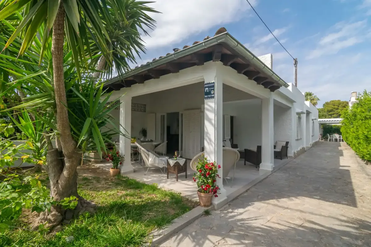 Una casa blanca con un patio cubierto junto a una entrada pavimentada.