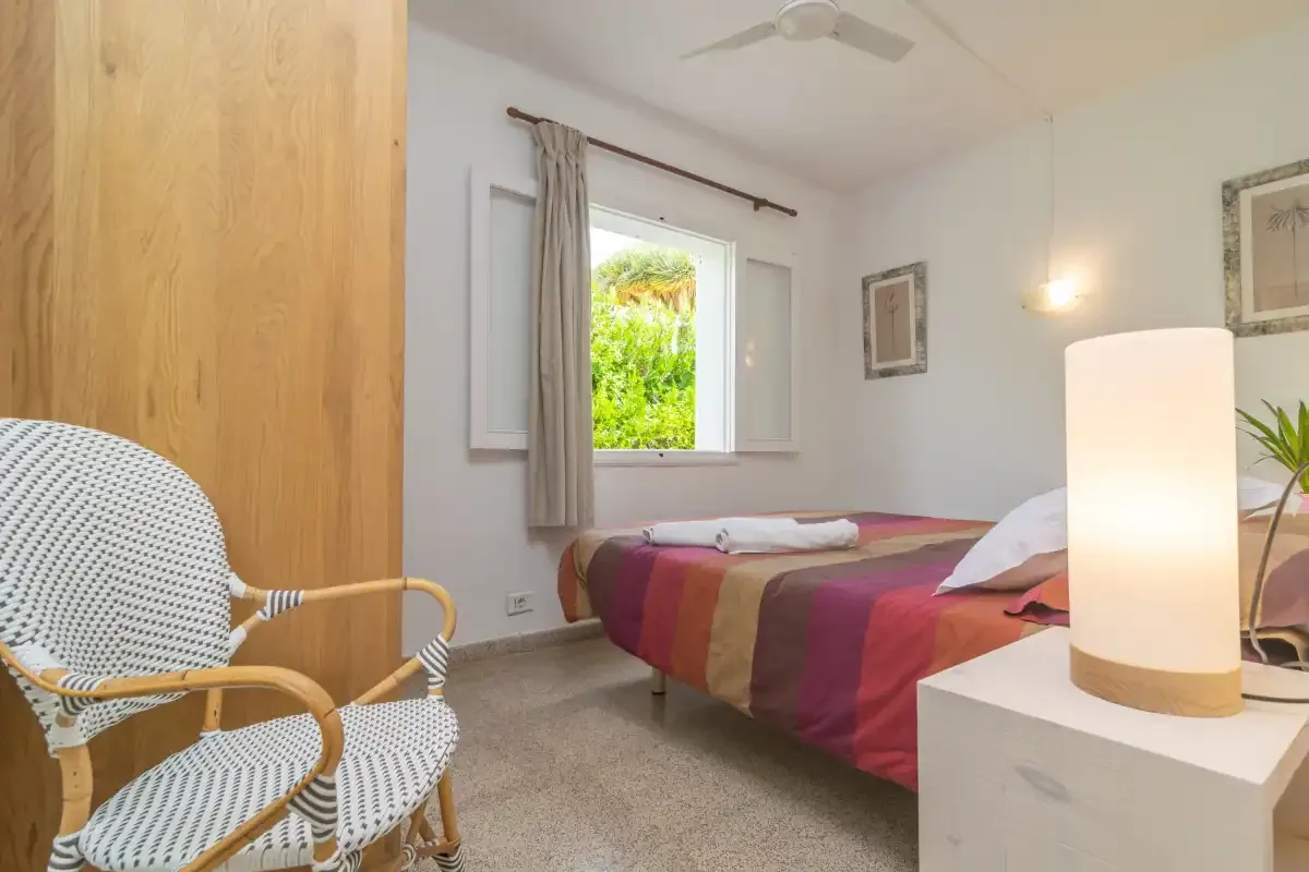Un dormitorio con una cama, un sillón estampado y una ventana con vistas a la vegetación.