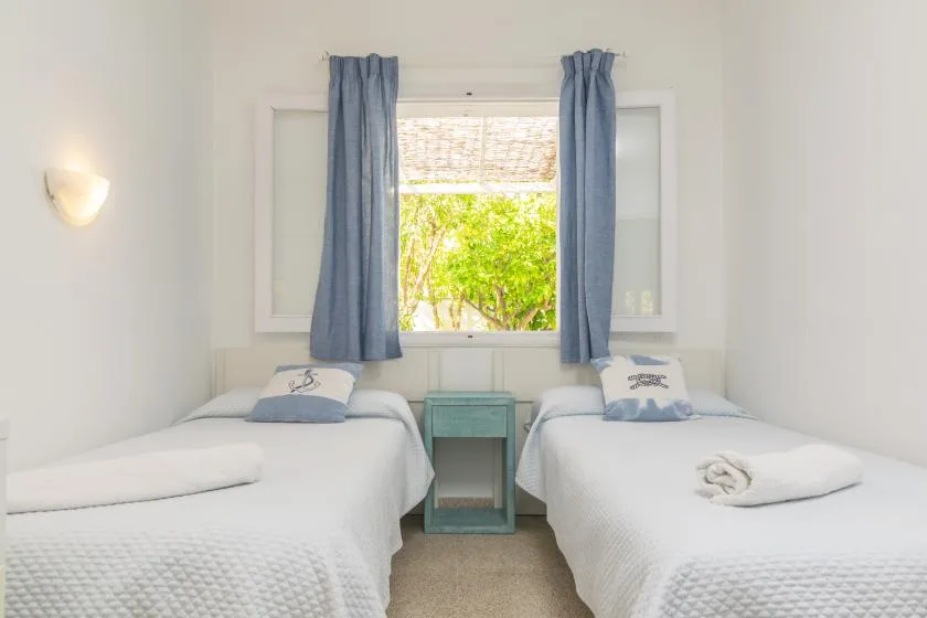 Un dormitorio luminoso con dos camas junto a una ventana con cortinas azules.