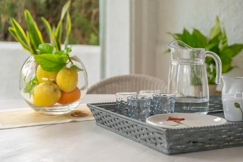 Una mesa está preparada con una bandeja de vasos, una jarra de agua y una composición de frutas.