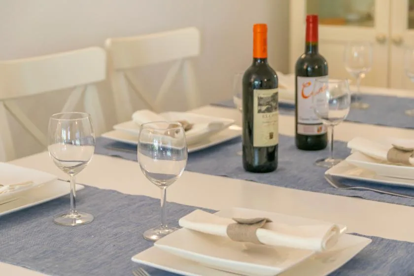 Una mesa de comedor está puesta con platos, copas y botellas de vino.