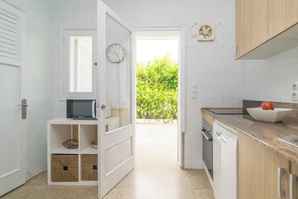 Una cocina luminosa se abre a través de una puerta hacia la vegetación exterior.