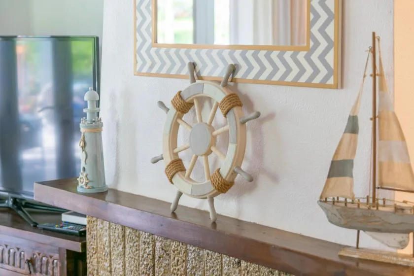 Una repisa de sala muestra un timón y un velero en miniatura junto a un televisor.