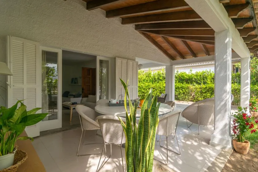 Un patio cubierto con asientos de comedor y vistas a un jardín frondoso.