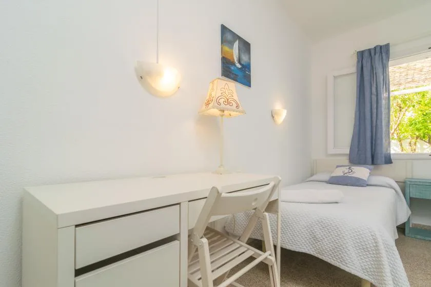 Un dormitorio luminoso con un escritorio junto a una cama y una ventana con cortina.